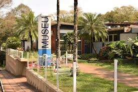 Entrada do Museu Antropológico com jardim, palmeiras e placa com a palavra Museu.